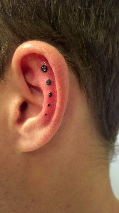 Tiny dot tattoo next to a helix piercing